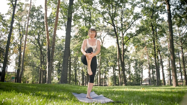 Foto di donna di mezza età in abiti sportivi che praticano yoga all'aperto al parco. Donna di mezza età che si allunga e medita nella foresta