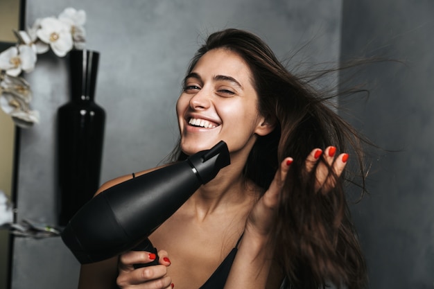 Foto di donna sorridente con lunghi capelli scuri e una pelle sana che si asciuga i capelli