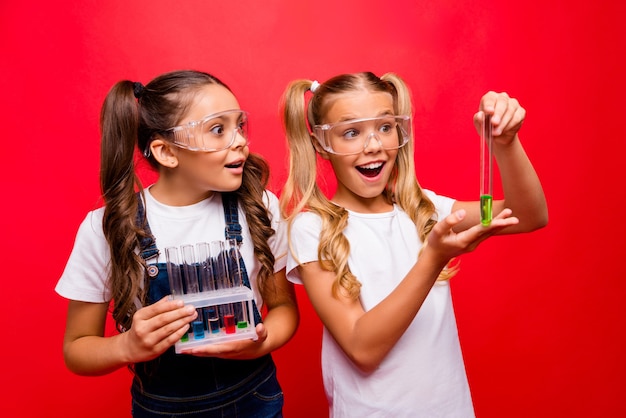 Foto di due divertenti piccole signore diligenti bambini della scuola fanno esperimenti chimici risultati entusiasmanti tenere il tubo indossare le specifiche di sicurezza t-shirt generale isolato colore rosso