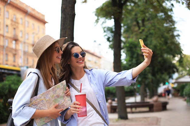 Foto di due ragazze che si godono le visite turistiche all'aperto. Belle turiste che esplorano la città con la mappa e si fanno selfie.