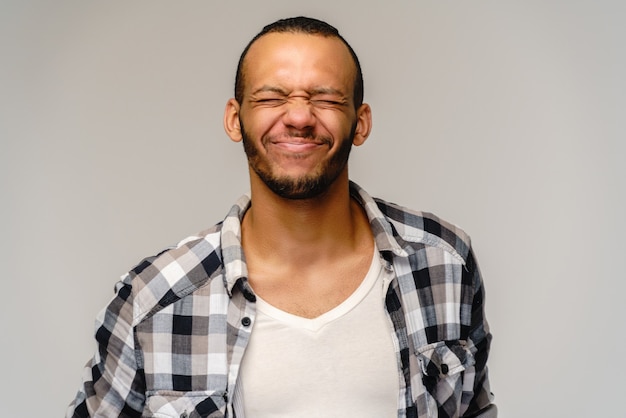 Foto di emotivo giovane afro-americano con gli occhi chiusi in piedi sul grigio.