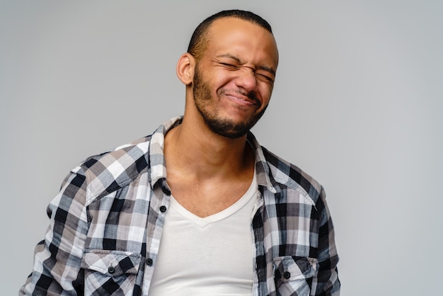 Foto di emotivo giovane afro-americano con gli occhi chiusi in piedi sul grigio.