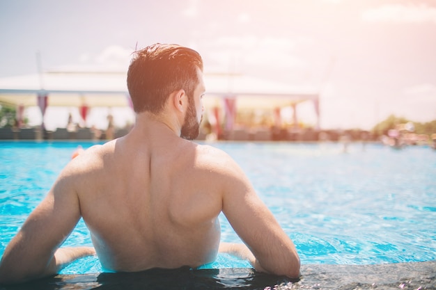 Foto di estate dell'uomo sorridente muscolare nella piscina. Modello maschio felice in acqua sulle vacanze estive