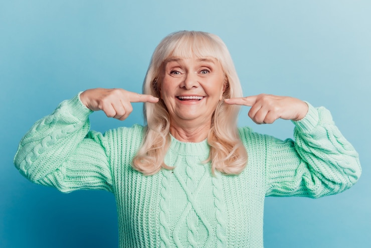 Foto di felice con sorriso raggiante donna pensionata punto denti bianchi isolati su sfondo blu