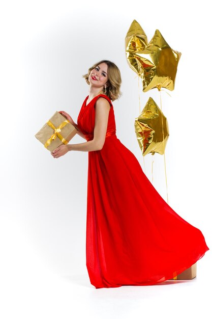 Foto di festa di eleganza signora sexy in abito rosso con labbra rosse e bei capelli ricci biondi, sorridente. Sfondo di mongolfiere e regali d'oro. Concetto della vendita