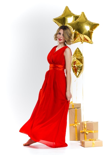Foto di festa di eleganza signora sexy in abito rosso con labbra rosse e bei capelli ricci biondi, sorridente. Sfondo di mongolfiere e regali d'oro. Concetto della vendita