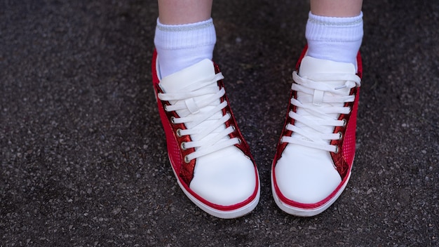 Foto di gambe femminili in scarpe da ginnastica rosse e bianche su asfalto bagnato grigio