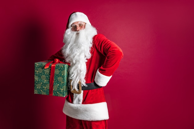 Foto di gentile Babbo Natale che presenta il regalo di Natale e che guarda l'obbiettivo