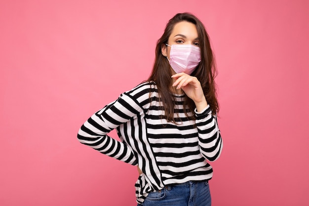 Foto di giovane bella donna con maschera protettiva riutilizzabile contro il virus sul viso contro il coronavirus isolato sul muro di sfondo rosa