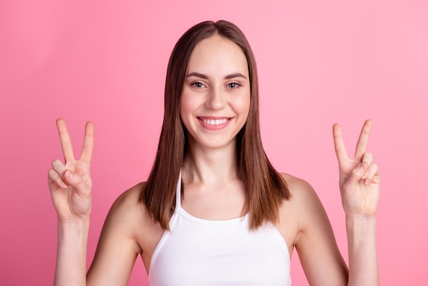 Foto di giovane donna attraente spettacolo allegro dita pace vittoria v-simbolo isolato su sfondo di colore rosa.