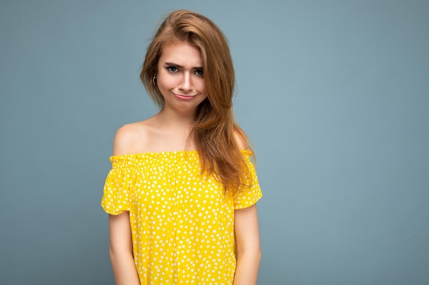 Foto di giovane donna bionda scura infelice divertente bella deliziosa deliziosa carina con sincere emozioni isolate sulla parete di fondo blu con lo spazio della copia per testo che indossa vestito giallo alla moda.