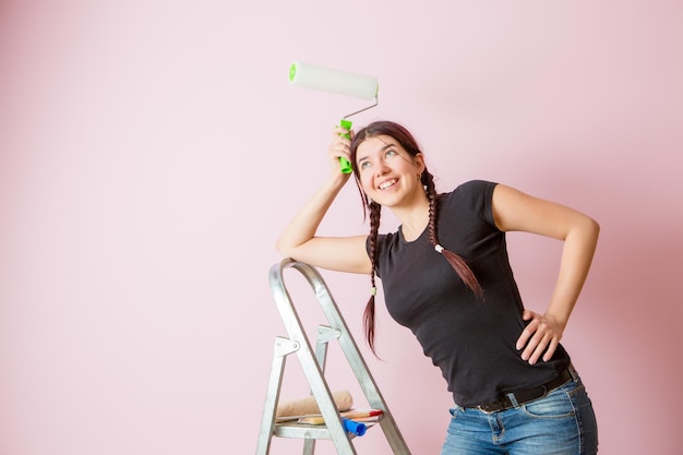 Foto di giovane donna con rullo di vernice in piedi vicino alla scala