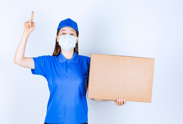 Foto di giovane donna in uniforme con scatola di carta che punta il dito verso l'alto.