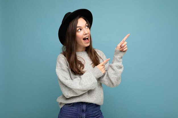 Foto di giovane donna scioccata positiva che dirige le dita di lato con uno spazio vuoto