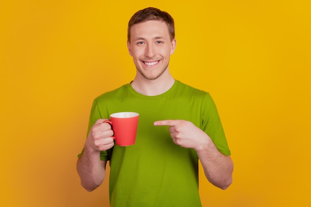 Foto di giovane uomo felice sorriso positivo punto dito tazza di caffè consiglio annuncio isolato su sfondo di colore giallo