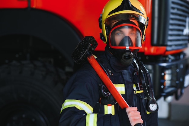 Foto di giovane vigile del fuoco con la mazza in mano vicino all'autopompa