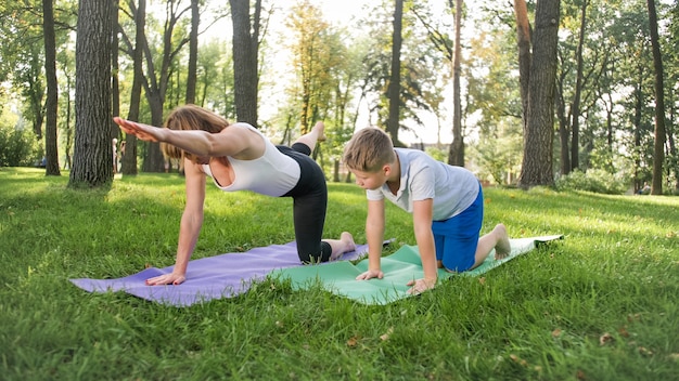 Foto di insegnante di yoga femminile di mezza età o guru che insegna a un adolescente che fa yoga. Donna con ragazzo che medita e si allunga sull'erba al parco
