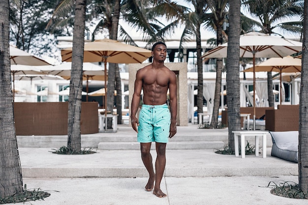 Foto di moda di un uomo atletico afroamericano con un corpo sportivo in posa vicino all'hotel e alle palme. Phuket. Tailandia.