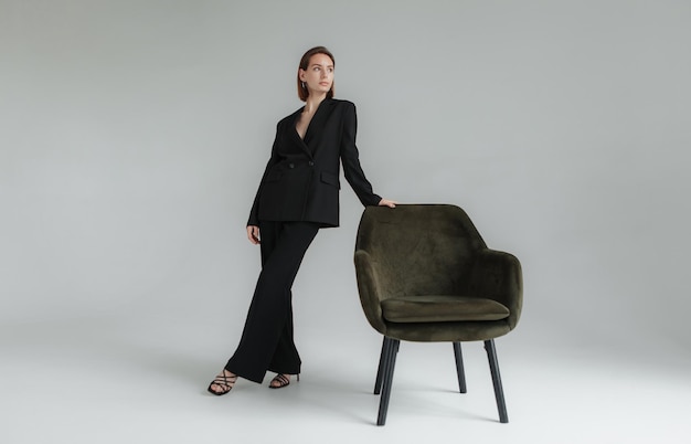 Foto di moda di una giovane donna elegante in abito nero con una poltrona nello studio Vogue Lifestyle