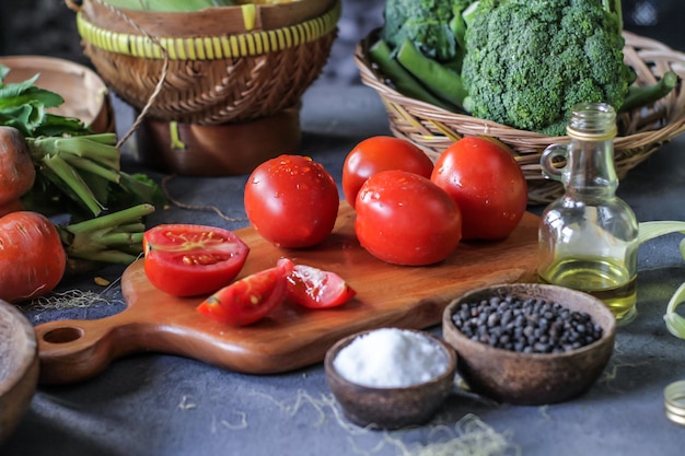 Foto di pomodori freschi nel tagliere, intorno a verdure, carote, sale, pepe nero, mais, broccoli. Tagliare i pomodori. Raccolta pomodori. Tavolo di legno.