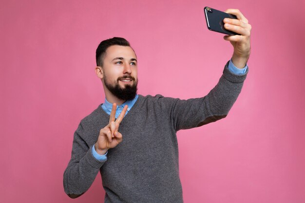 Foto di positivo bello giovane uomo con la barba lunga bruna con la barba che indossa un maglione grigio casual