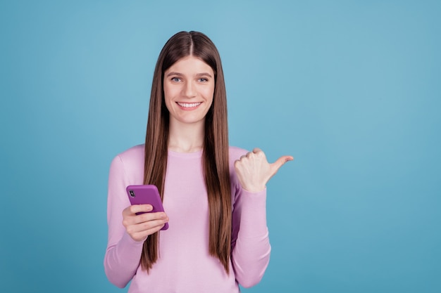Foto di ragazza allegra eccitata punta pollice spazio vuoto annuncio pubblicitario seleziona promo cellulare isolato sfondo di colore blu