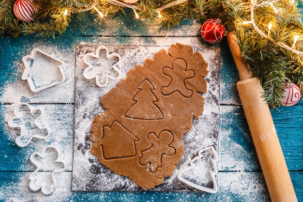 Foto di rami di pino, pasta, stampi per biscotti, mattarello sulla tavola di legno blu