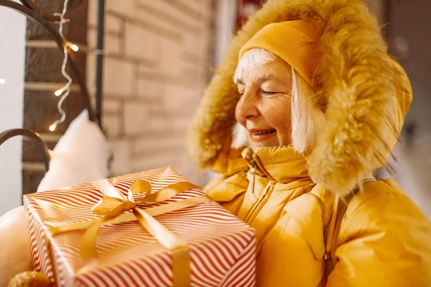 Foto di shopping natalizio di una donna matura allegra che indossa abiti caldi con in mano un regalo di Natale...