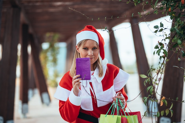 Foto di stock di mama noel che mostra un regalo con una mano e sacchetti regalo nell'altra. periodo natalizio