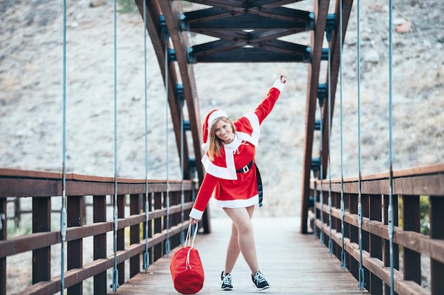 Foto di stock di Mama Noel giocando felicemente con la borsa rossa di regali su un ponte di legno Natale