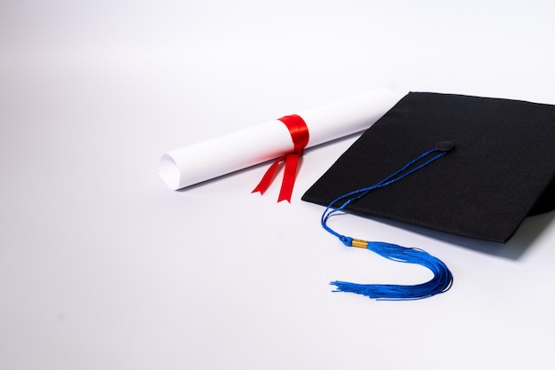 Foto di stock di un tappo di graduazione mortaio bordo e certificato di diploma isolato su sfondo bianco con copia negativa spazio per aggiungere del testo. Cappello di laurea con diploma sul tavolo su sfondo bianco