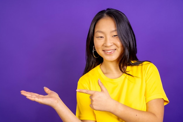Foto di studio con sfondo viola di una donna cinese positiva che punta verso il lato