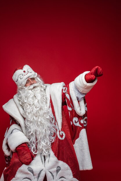 Foto di studio di Babbo Natale dalla barba bianca in costume rosso e bianco con una lunga barba bianca rivolta verso l'esterno con il braccio.