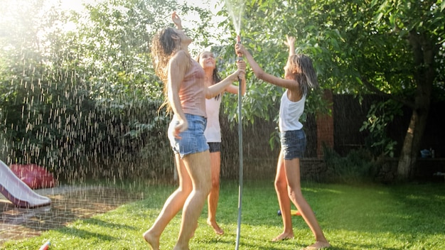 Foto di tre ragazze adolescenti allegre che ballano nel giardino sul retro del tubo dell'acqua del giardino udner