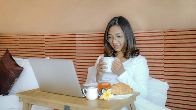 Foto di turisti che mangiano colazione e laptop utilizzato sul letto nella camera d'albergo di lusso, concetto di cibo sano.