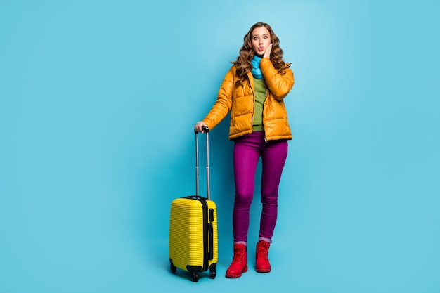 Foto di tutto il corpo della bella signora viaggiatore tenere la borsa da viaggio attendere la registrazione del volo dell'aeroporto lunga coda grande indossare cappotto giallo sciarpa blu pantaloni scarpe isolato muro di colore blu