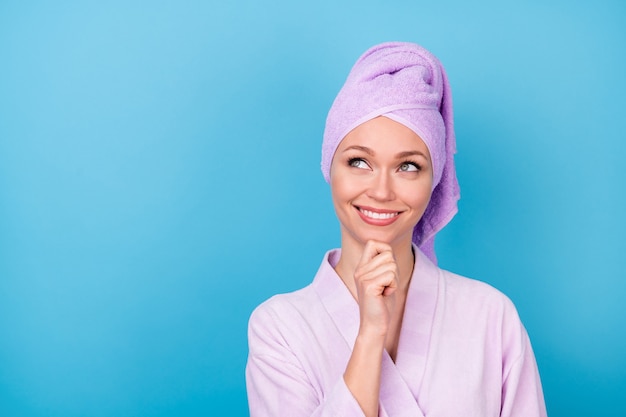 Foto di un'affascinante ragazza con il mento del braccio cerca lo spazio vuoto sorriso lucido indossa un asciugamano viola turbante accappatoio isolato sfondo blu colore