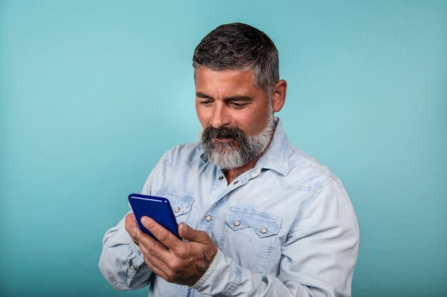 Foto di un allegro uomo barbuto che usa il suo smartphone su sfondo blu