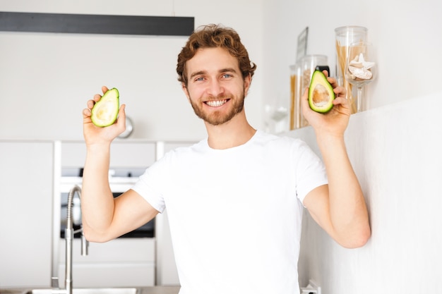 Foto di un bel giovane in cucina a casa che cucina tenendo avocado.
