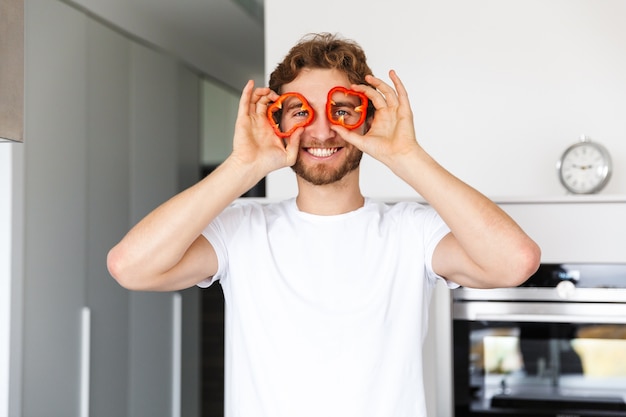 Foto di un bel giovane in cucina a casa che cucina tenendo la paprica di pepe