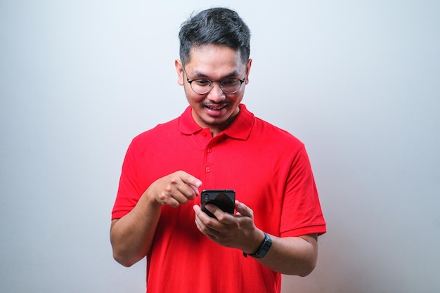 Foto di un bell'uomo allegro positivo che indossa una camicia casual che tiene e indica lo smartphone sorridente alla ricerca di informazioni