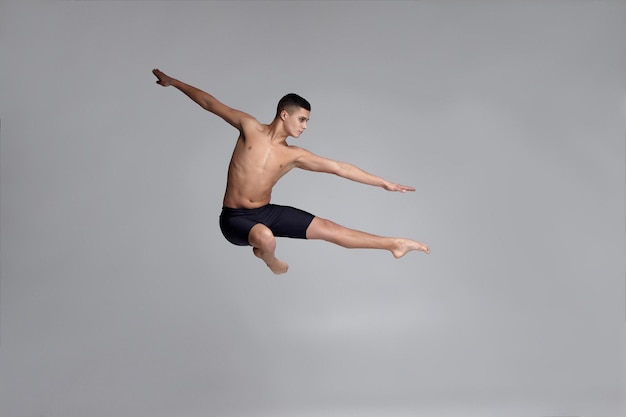 Foto di un bell'uomo ballerino vestito con pantaloncini neri che fa un elemento di danza contro un gra...