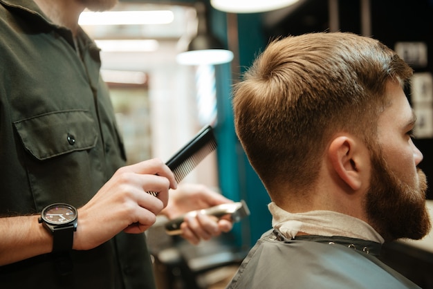 Foto di un giovane che si fa tagliare i capelli dal parrucchiere con il rasoio mentre è seduto in poltrona. Guardare oltre.