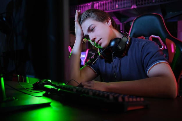 Foto di un giovane giocatore caucasico professionista che gioca online sul suo PC in un club di gioco o in una cyber arena. Sembra dispiaciuto e sconvolto. Il piano di gioco è andato storto