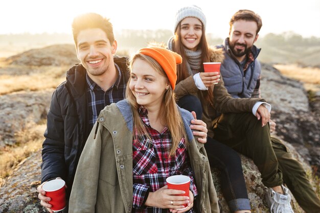 Foto di un giovane gruppo di amici fuori in vacanza alternativa gratuita in campeggio sulle montagne che bevono tè caldo e parlano tra loro.