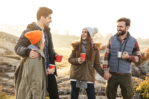 Foto di un giovane gruppo di amici fuori in vacanza alternativa gratuita in campeggio sulle montagne che bevono tè caldo e parlano tra loro.