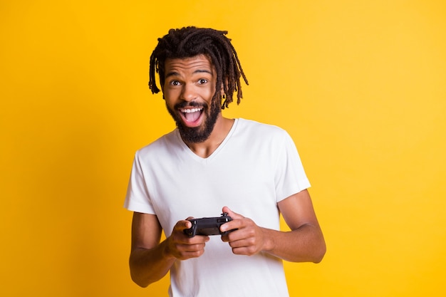 Foto di un giovane ragazzo nero che tiene il controller con il joystick a bocca aperta indossa una maglietta bianca isolato sfondo di colore giallo