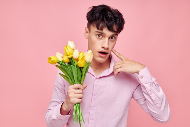 Foto di un giovane ragazzo romantico con una maglietta rosa con un mazzo di fiori che fa gesti con le mani Stile di vita inalterato