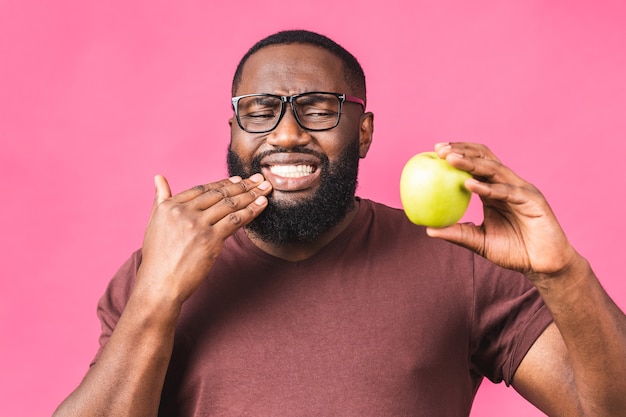 Foto di un giovane uomo di colore afroamericano isolato su sfondo rosa che soffre di un terribile dolore ai denti, mostrandolo vividamente sul viso, con un aspetto turbato e angosciato.