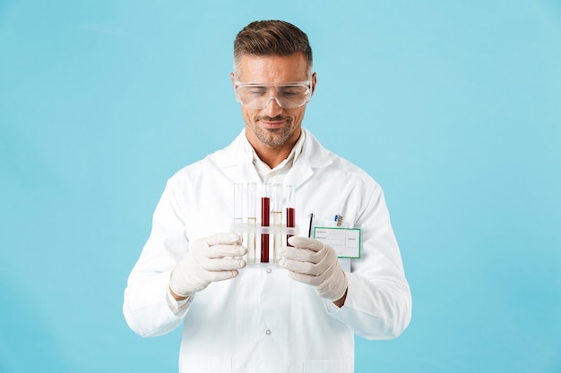 Foto di un medico di bell'uomo maturo in posa isolata sopra la parete blu che tiene le provette con sangue.